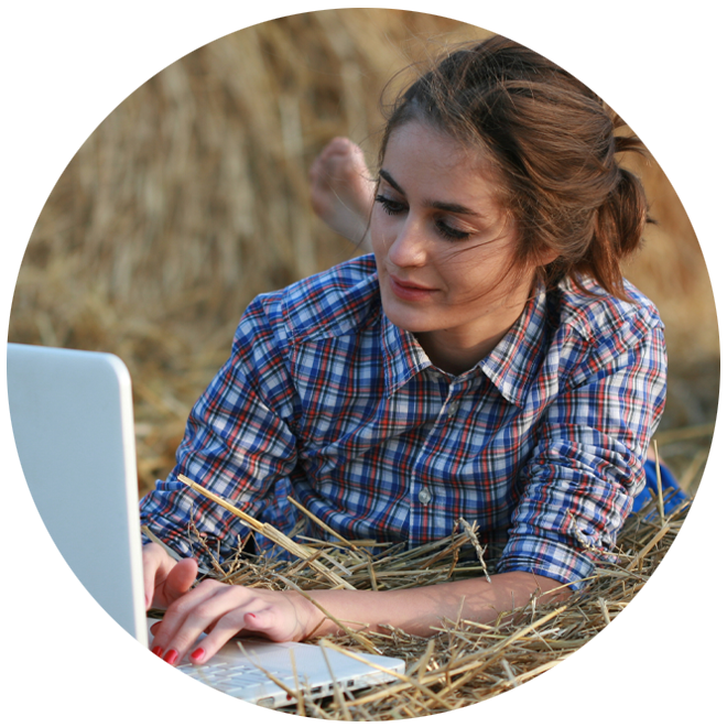 young woman using laptop laying outside on straw